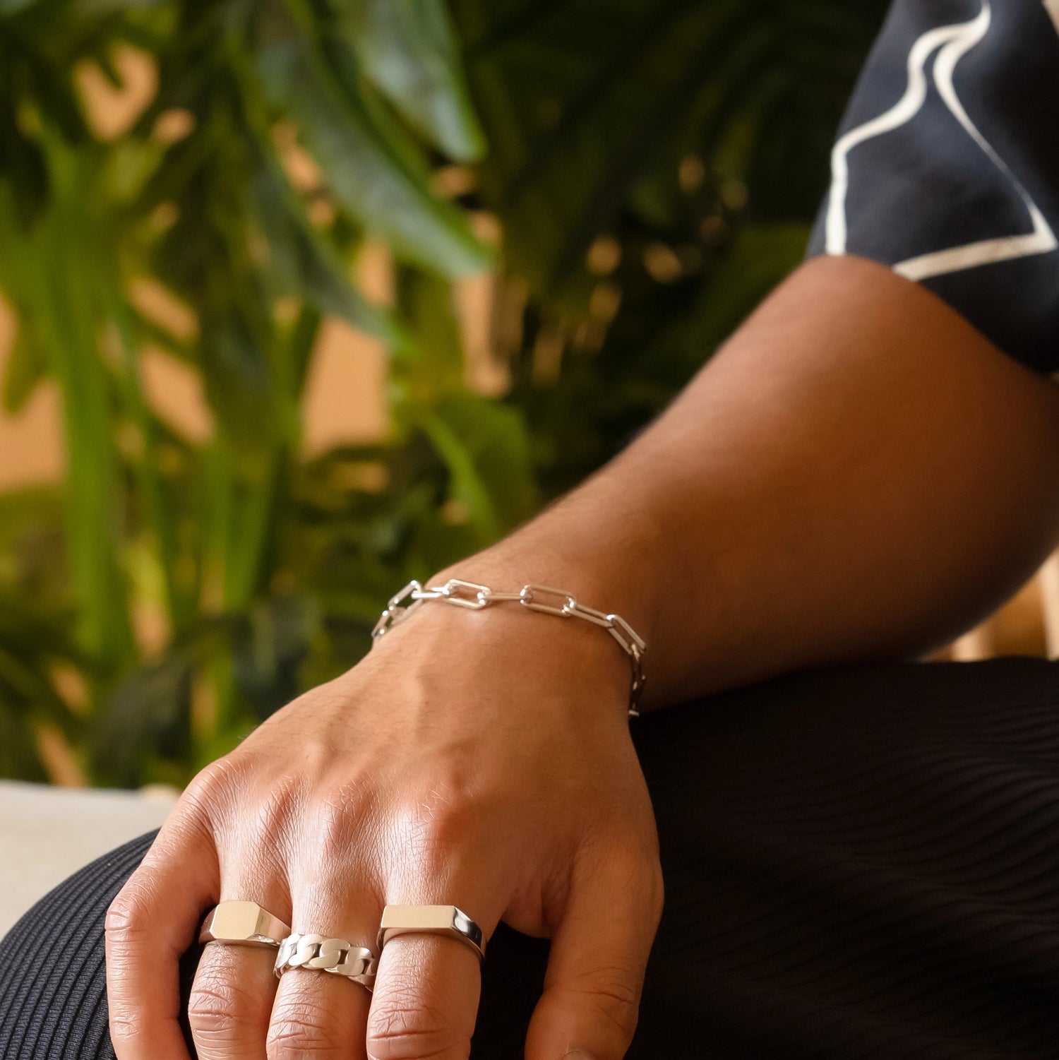 925 silver paperclip bracelet on right hand resting on plissé pants